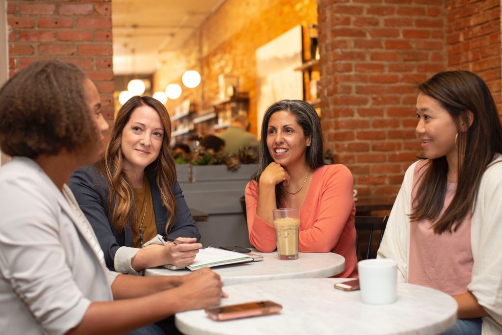 Four women talking in a coffee shop post-pandemic