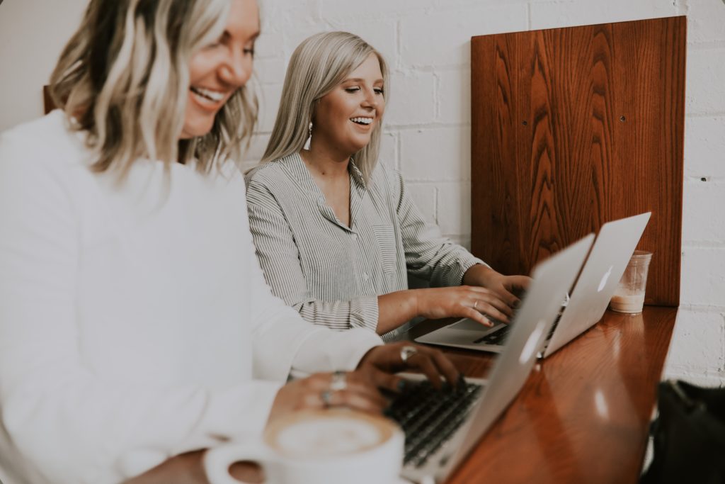 Two smiling women on laptops in coffee shop