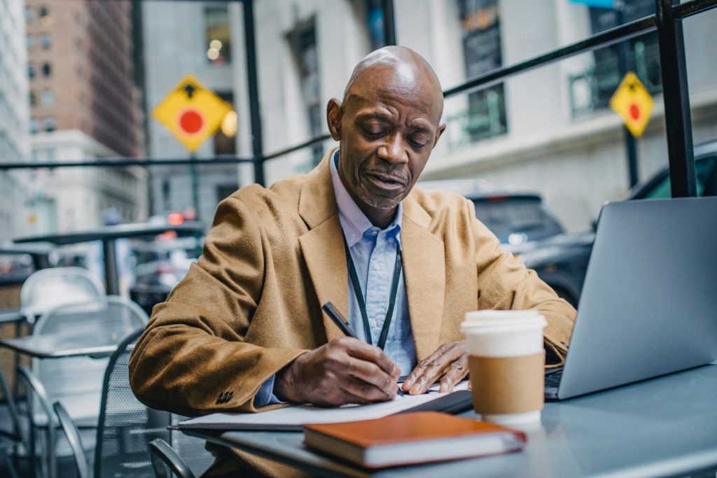 Older Black man writing during one-on-one meeting outside