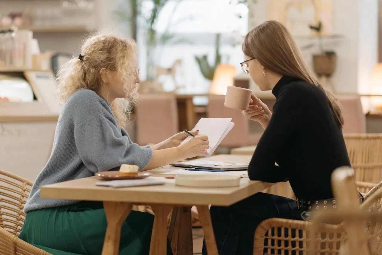 two-young-professional-women-exchanging-notes-at-coffee-shop Two women colleagues doing quarterly performance review