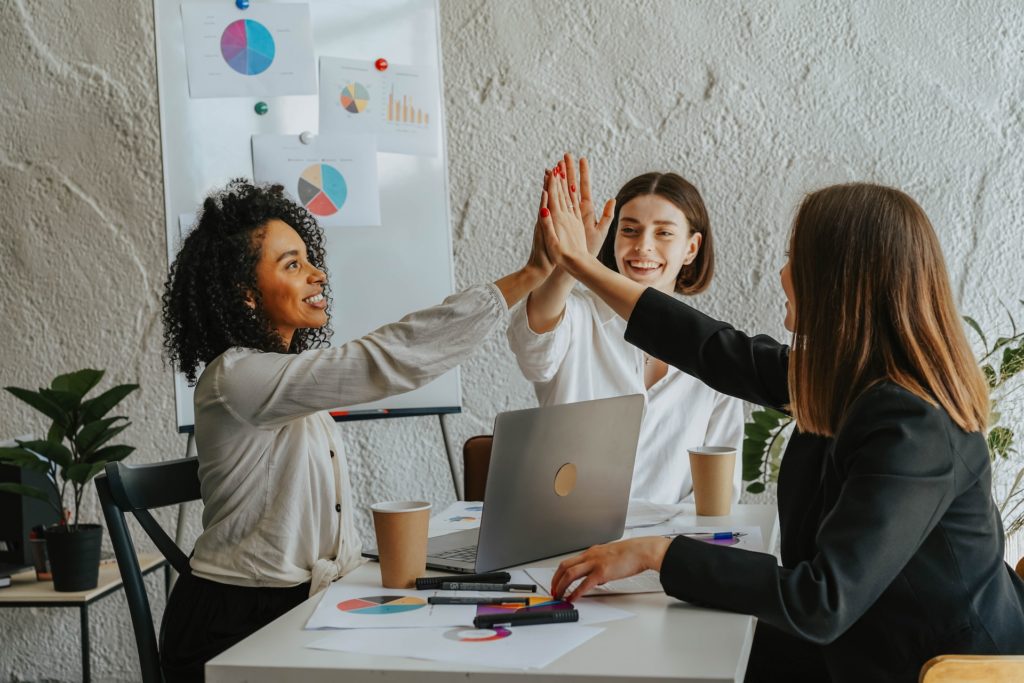 Three women colleagues high-fiving after leadership values meeting