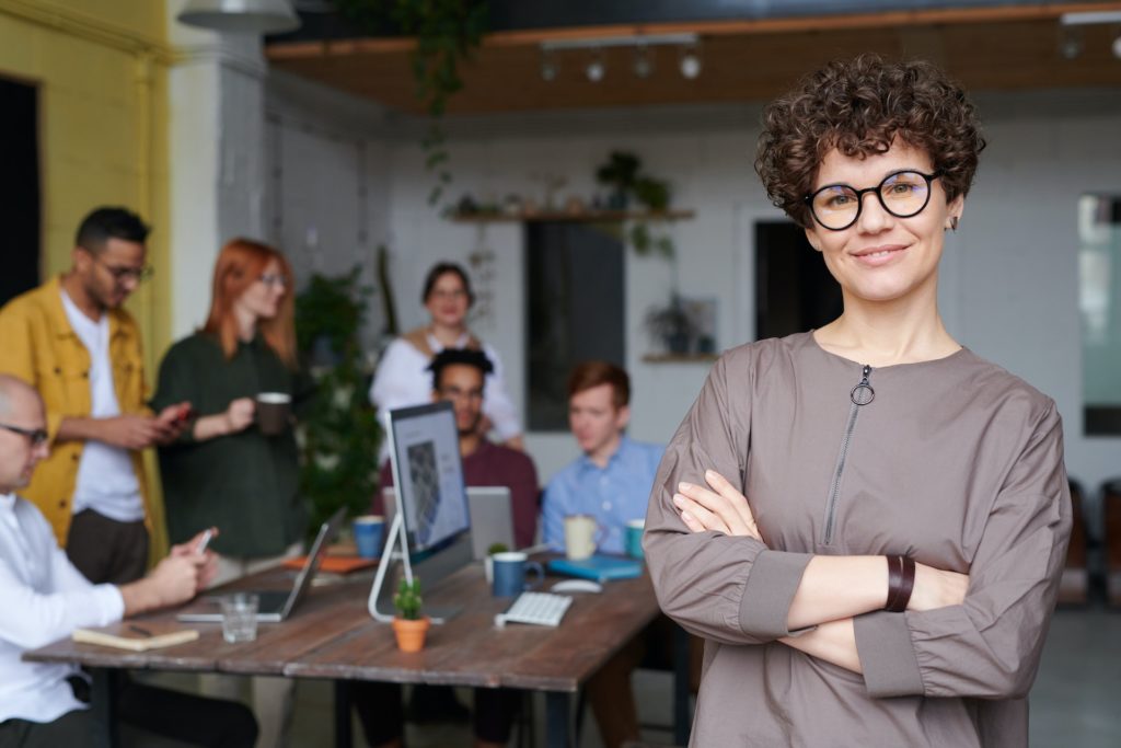 Woman smiling while diverse colleagues discuss strategy execution in the background