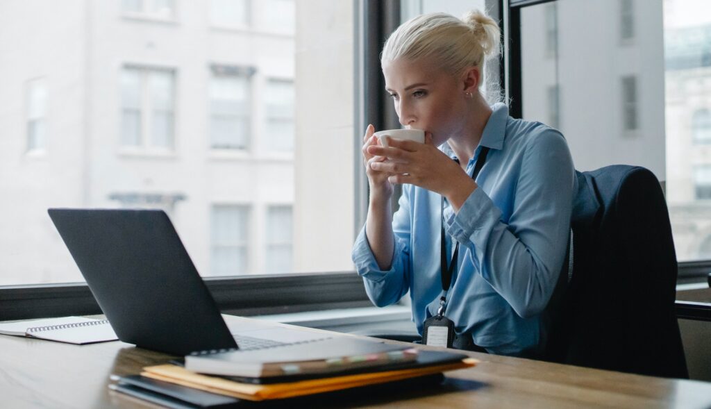 Woman drinking hot drink looking at 9 box grid on laptop
