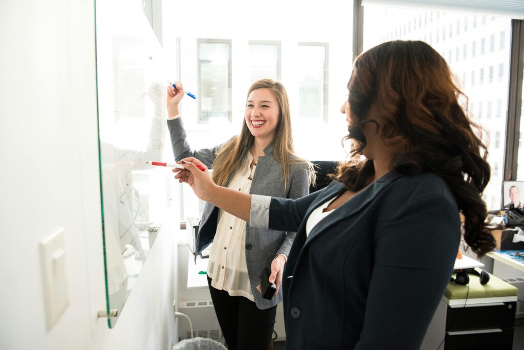 Two women brainstorming in front of a white board.