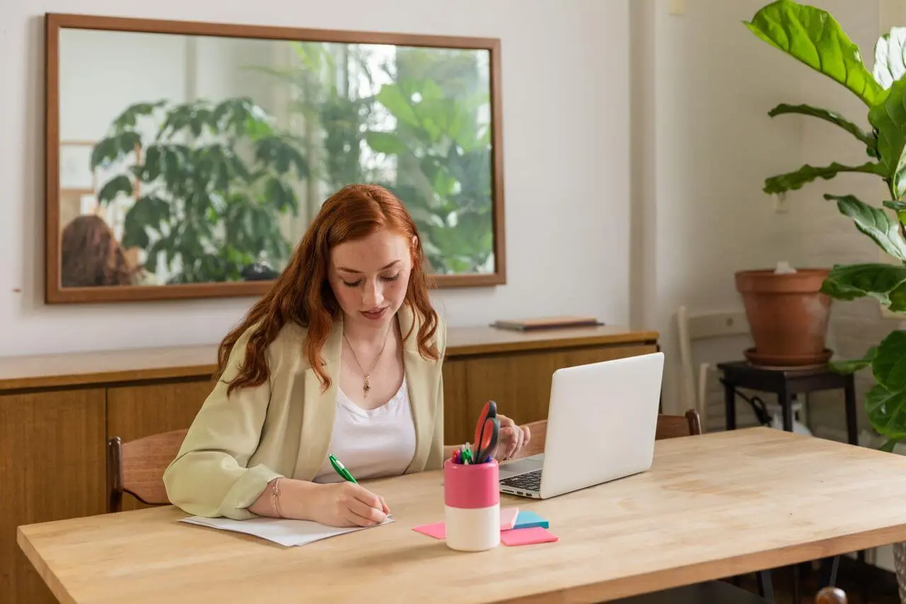 red-haired-woman-writing-at-desk-with-laptop